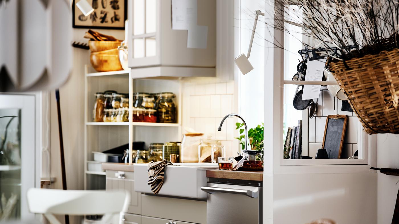 A beige country-style kitchen with a STENSUND unit with a white sink, and open and closed shelving with jars and utensils.