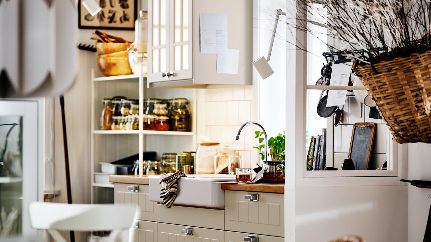 A beige country-style kitchen with STENSUND fronts on METOD cabinets, a white sink and shelving with jars and utensils.