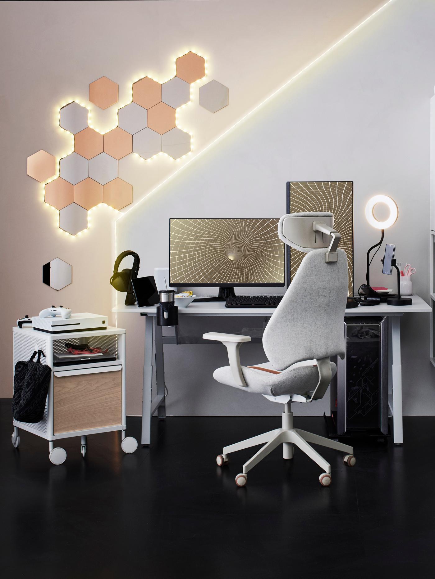 A beige IKEA GRUPPSPEL gaming chair in front of a desk with a screen and a drawer unit with accessories.