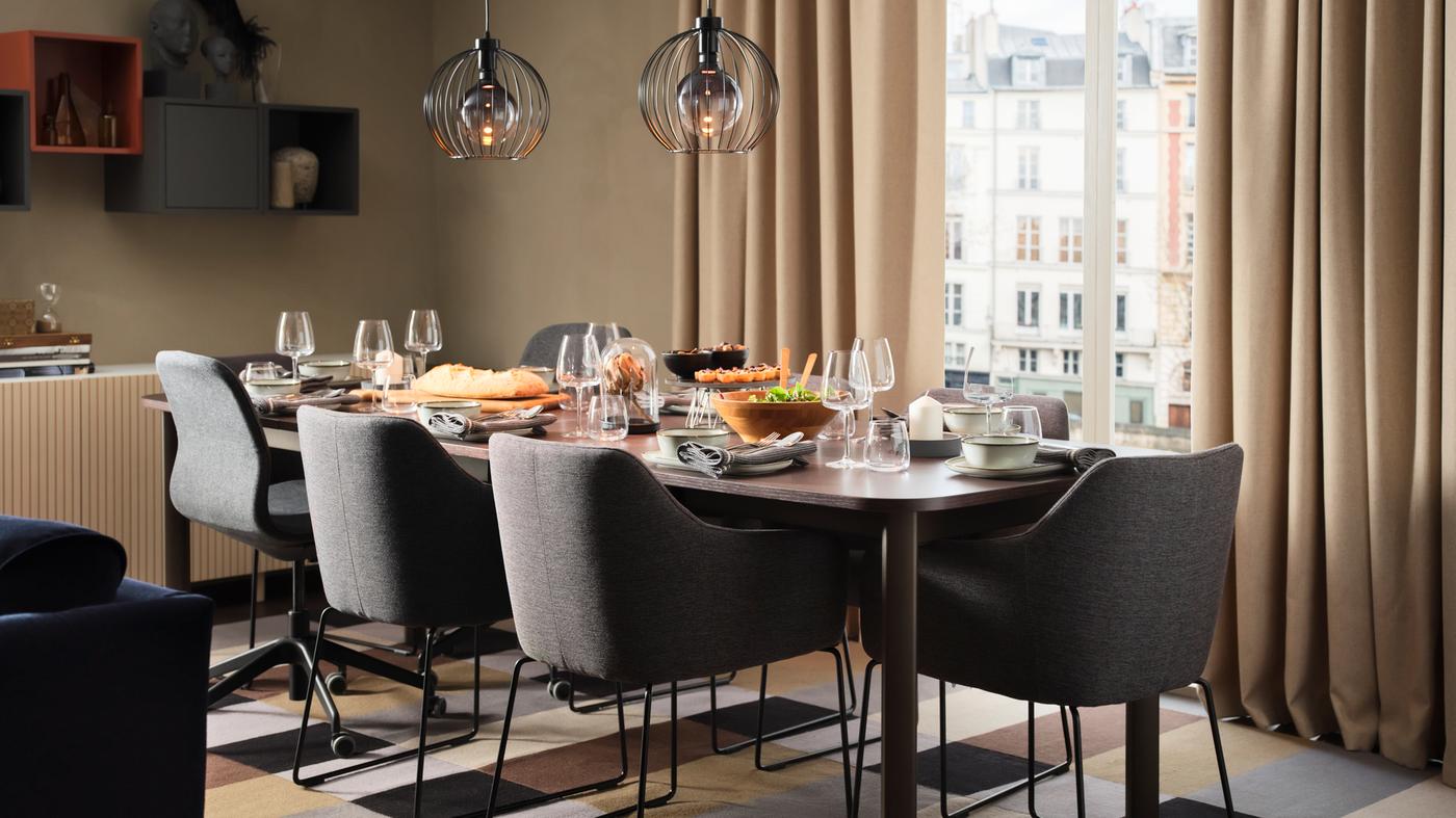 A beige living room with a STRANDTORP extendable table set for dinner surrounded by TOSSBERG and LÅNGFJÄLL chairs.