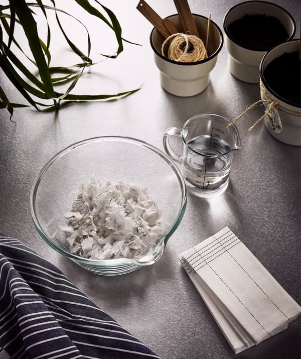 A beige plant pot, a brown notebook, textile napkins and paper napkins with home-made plant pods tied around them.