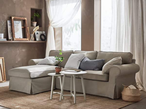 A beige sofa sectional with a chaise lounge in a living room with white curtains and tan walls
