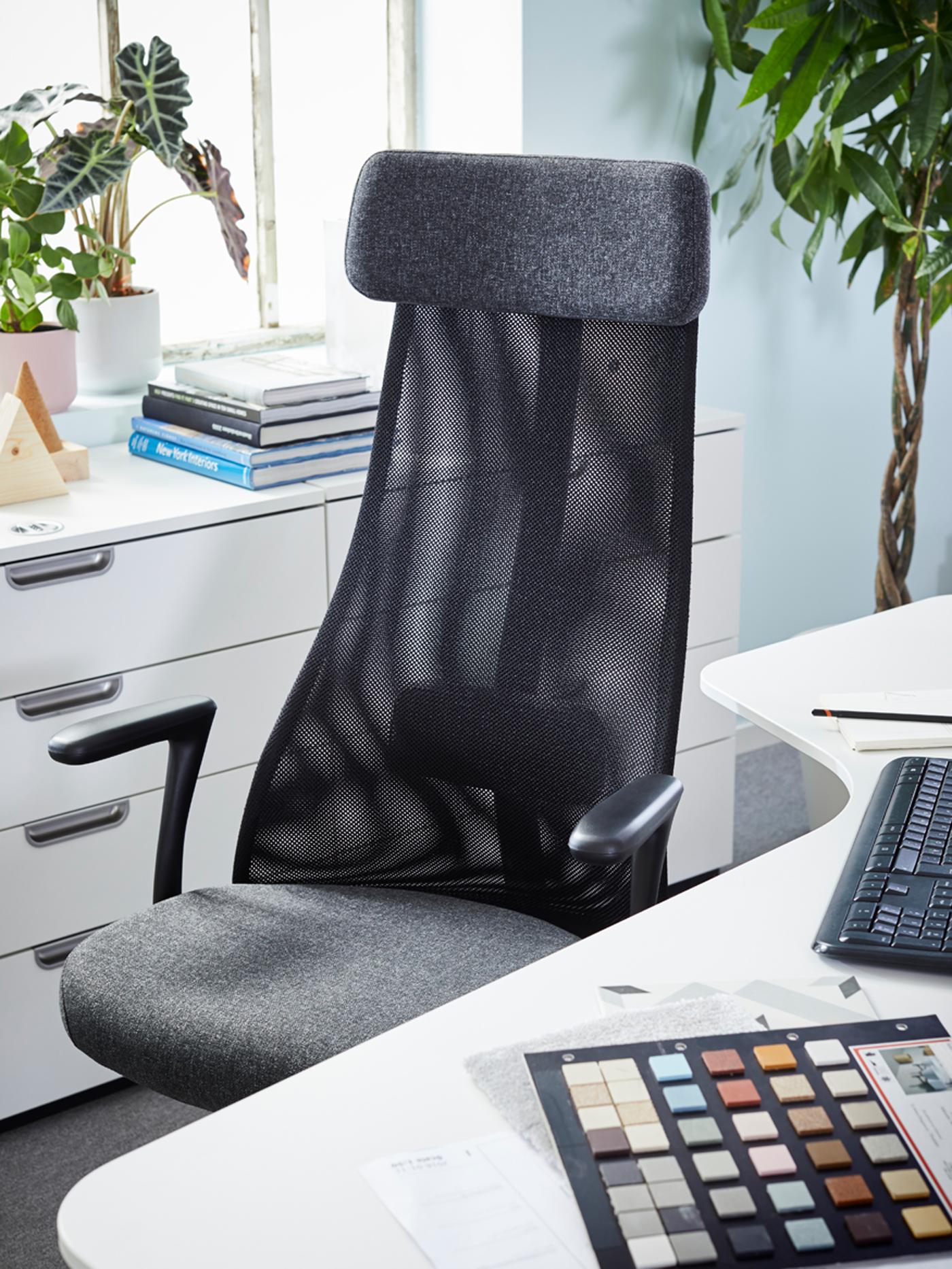 A BEKANT corner desk and a dark grey JÄRVFJÄLLET office chair by a window with potted plants and a pile of books.