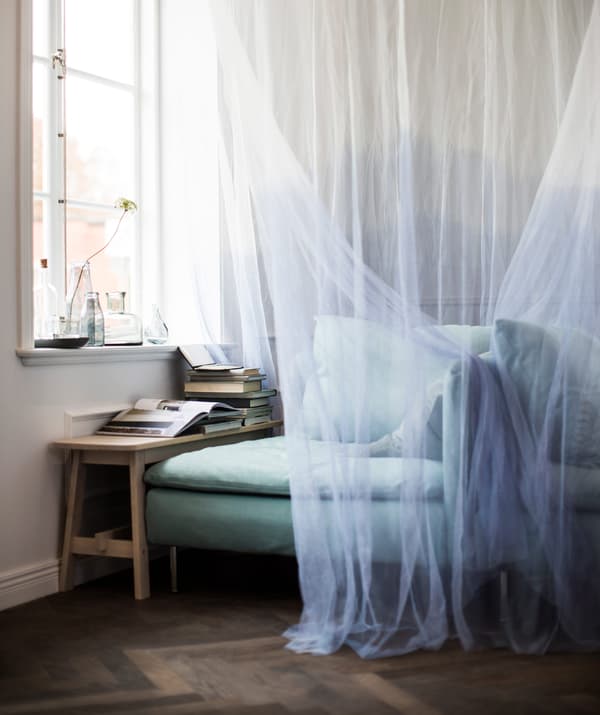 A bench and an IKEA SÖDERHAMN corner section are placed in front of a window and draped with a canopy to make a cosy reading space.