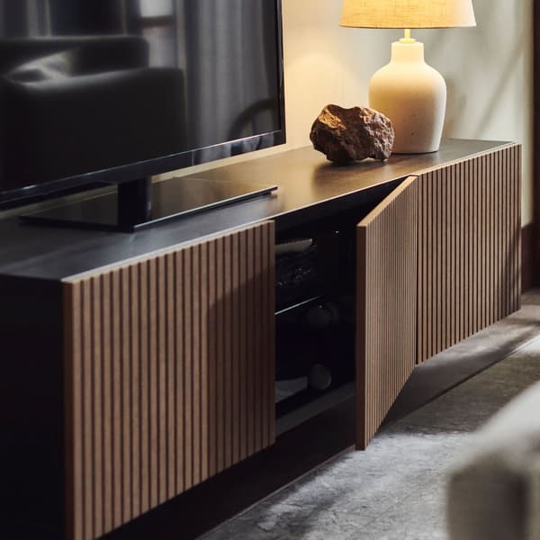 A BESTA TV cabinet with brown doors with a TV and a table lamp on top.