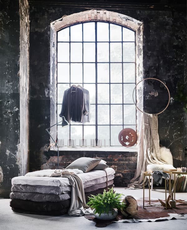 A big industrial loft window surrounded by softness with rugs, lots of throws and a sofa made from mattresses.