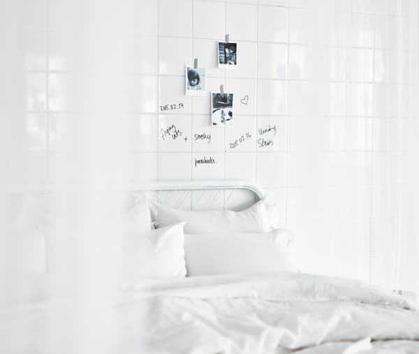 A big white bed against a glossy tiled wall, with small Polariod pictures and handwritten notes scrawled onto the wall.