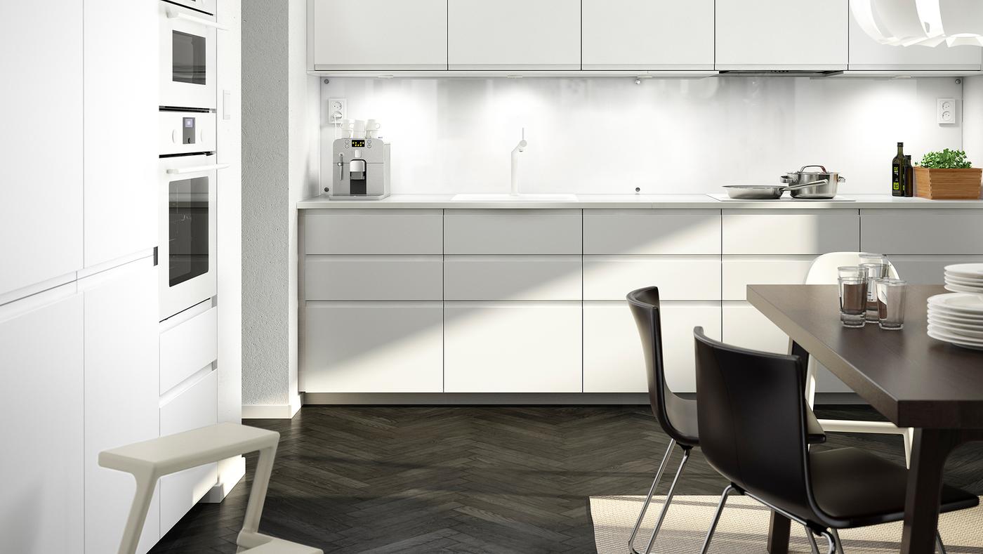 A big white kitchen with matte white kitchen doors and drawer fronts, a white worktop and a dark brown table with two chairs.