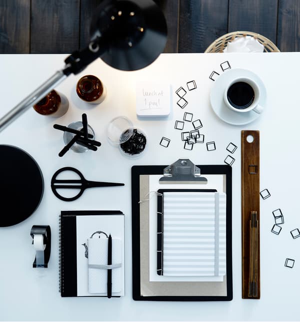 A bird’s-eye view of a home office desk with work supplies like paperclips, pens, and coffee.
