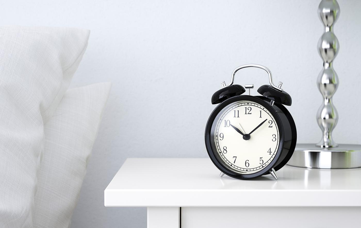 A black alarm clock on a bedside table.