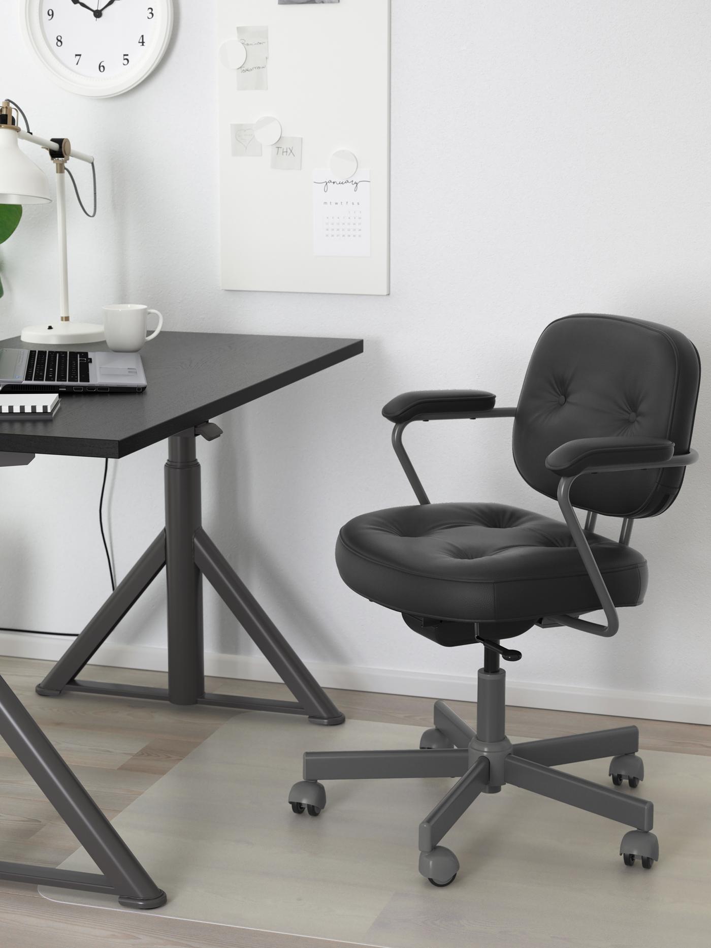 A black ALEFJÄLL office chair forms a workspace together with an IDÅSEN desk in a light, white-walled room.