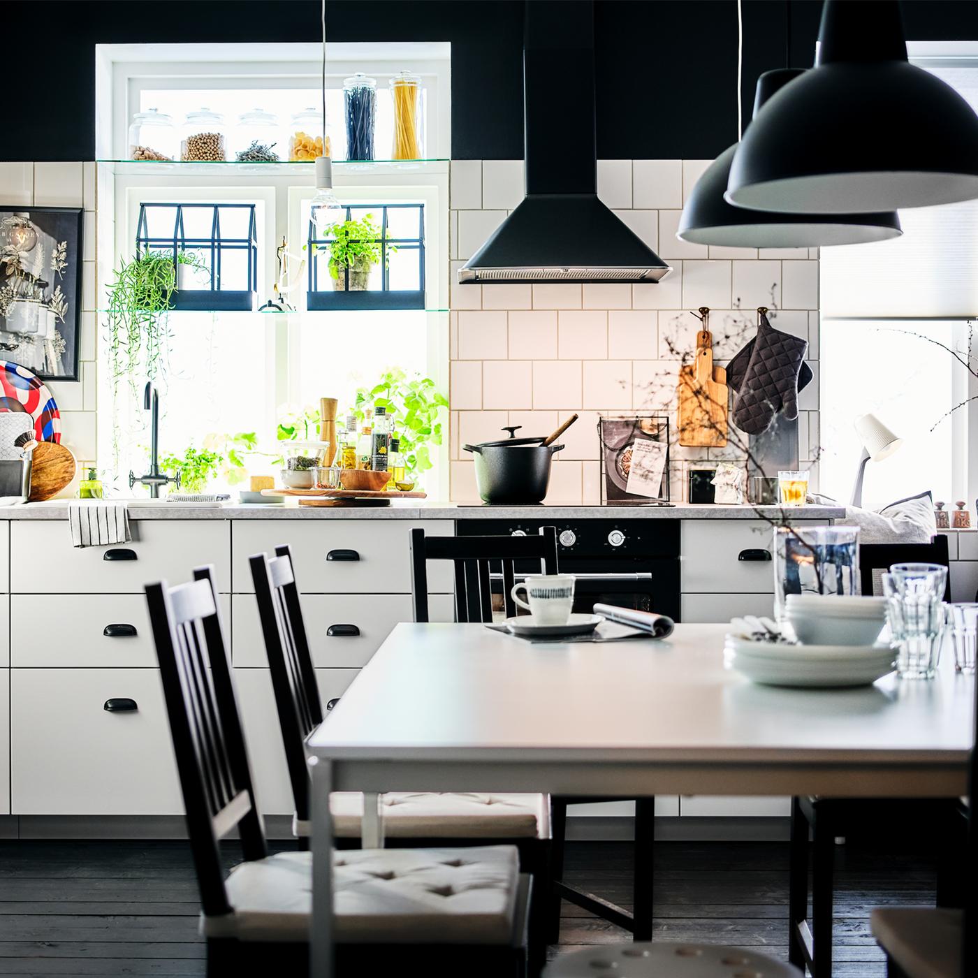 A black-and-white kitchen with white cabinets and a dining area centred around two white MELLTORP tables.
