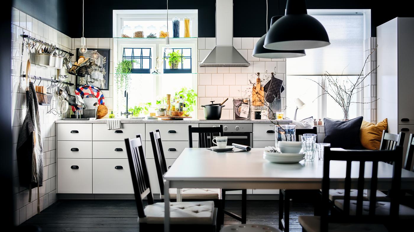 A black-and-white kitchen with white METOD cabinets with MAXIMERA interiors and a dining area with two white MELLTORP tables.