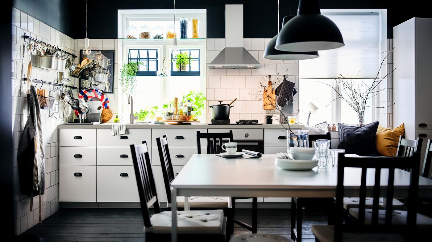 A black-and-white kitchen with white METOD cabinets with MAXIMERA interiors and a dining area with two white MELLTORP tables.