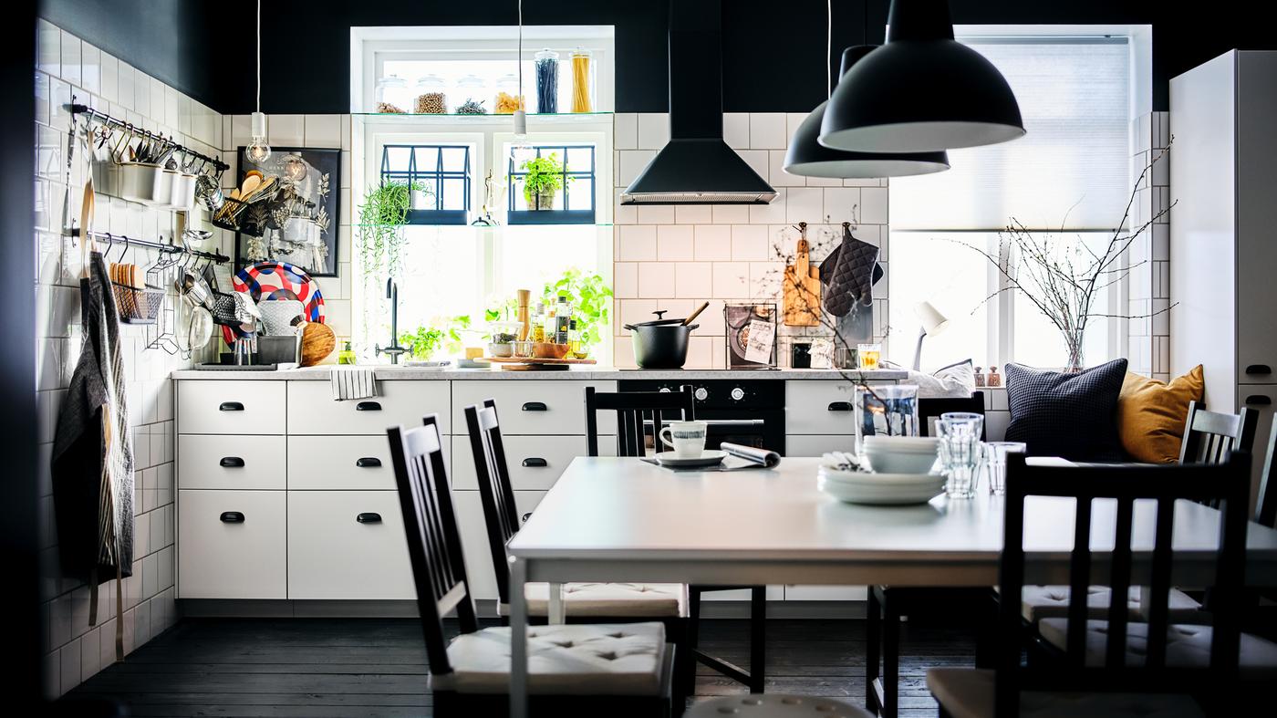 A black-and-white kitchen with white METOD cabinets with MAXIMERA interiors and a dining area with two white MELLTORP tables.