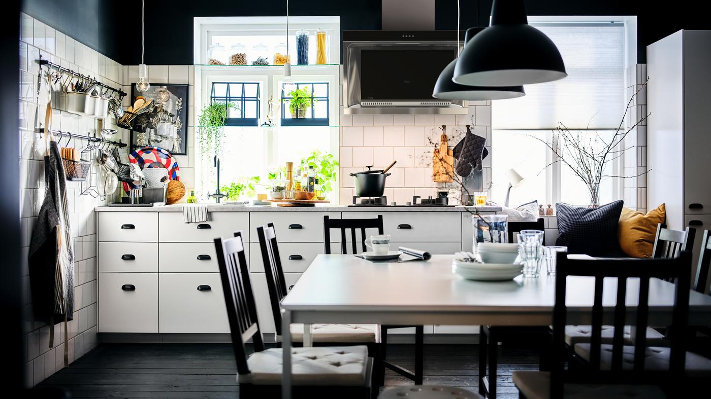 A black-and-white kitchen with white METOD cabinets with MAXIMERA interiors and a dining area with two white MELLTORP tables.