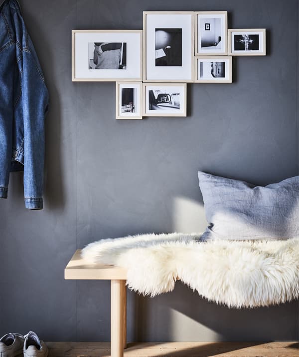 A black and white photo display hanging on a grey wall above a bench covered in a sheepskin.