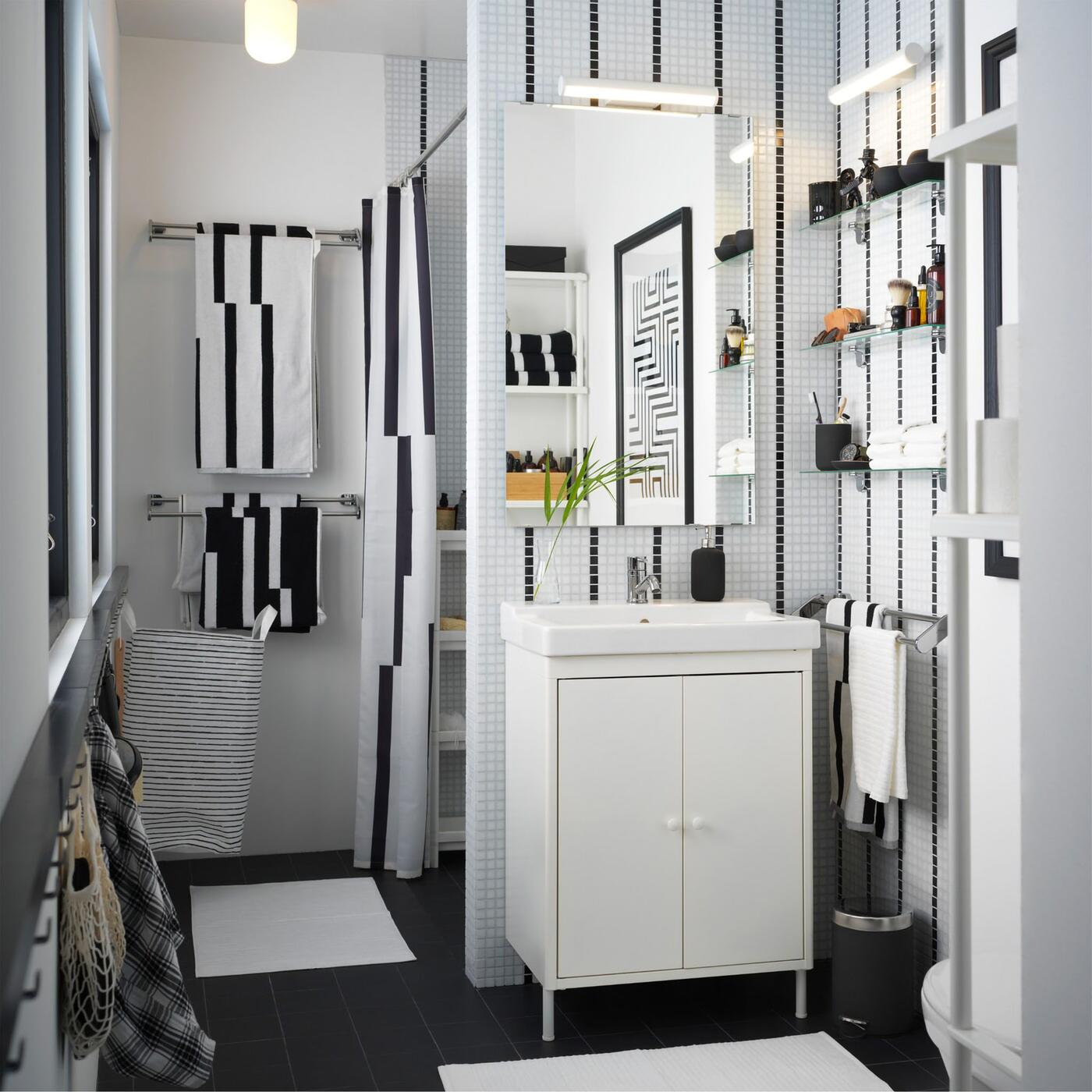 A black and white small bathroom with a white wash basin, striped towels, and a striped shower curtain.