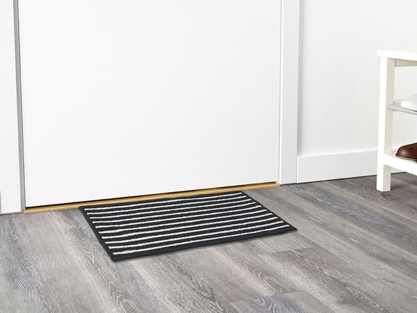 A black and white striped door mat on a gray wooden floor in front of a white doorway.