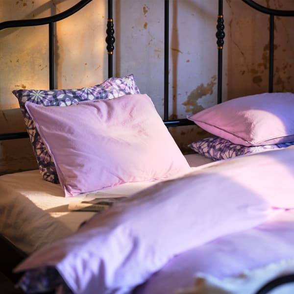 A black bed with a steel frame and brass-coloured details. The bed is placed against a rustic beige wall.