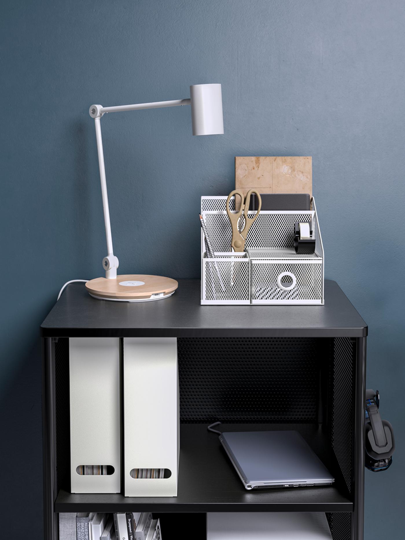 A black BEKANT storage unit on castors with a white RIGGAD LED work lamp and a white DRÖNJÖNS desk organiser on top.
