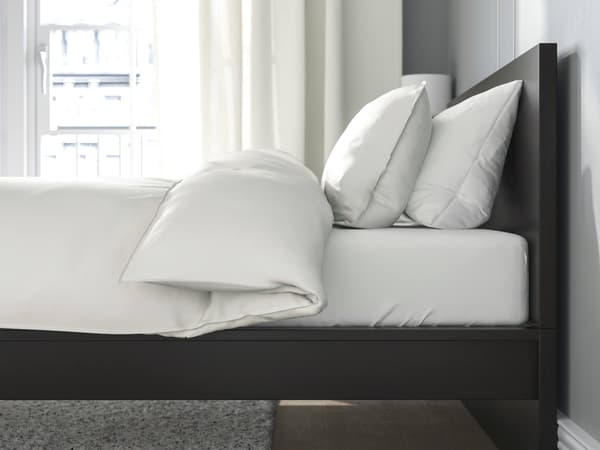A black-brown bed frame with white bedding on it.