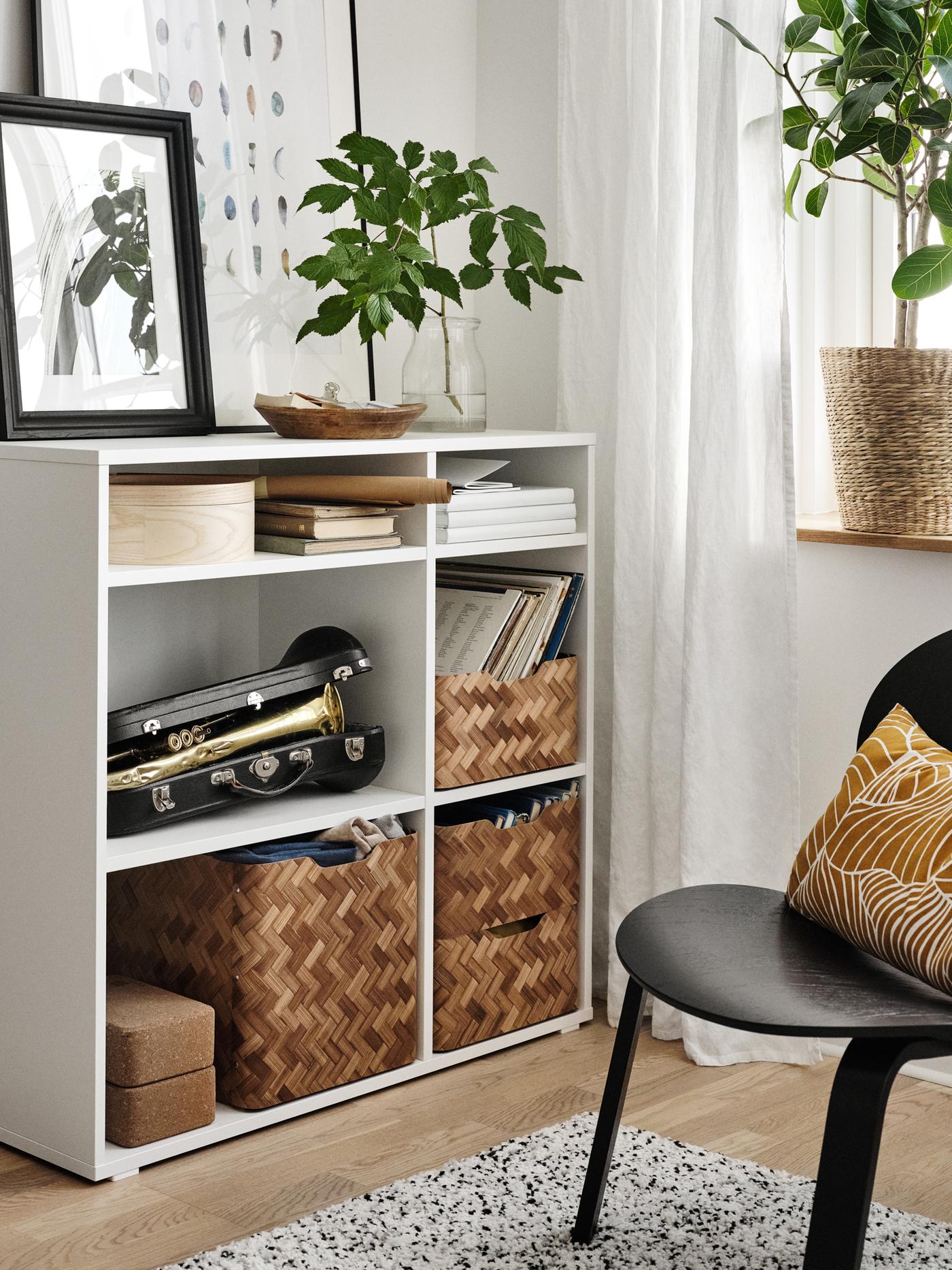 A black FRÖSET chair with a dark yellow cushion on it beside an open shelving unit holding baskets, books and a trumpet.