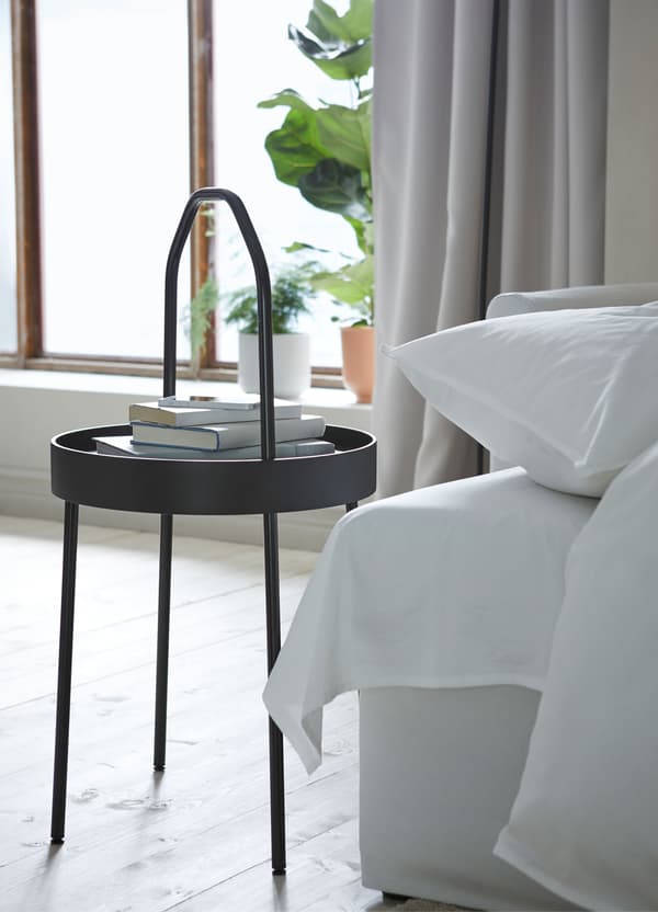 A black IKEA BURVIK circular side table with a thin lightweight handle, in a living room.