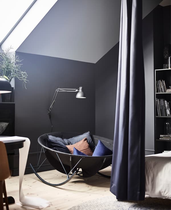 A black IKEA PS 2017 rocking-chair creates a reading corner in a bedroom with black walls.