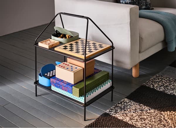 A black IKEA YPPERLIG magazine stand next to a cream sofa, stacked with board games.