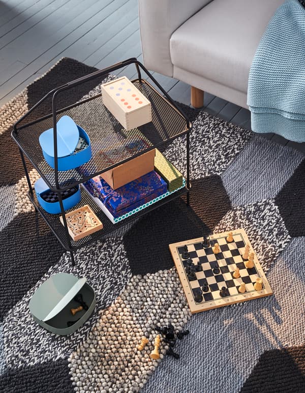 A black IKEA YPPERLIG magazine stand used to hold board games on a black and grey rug.