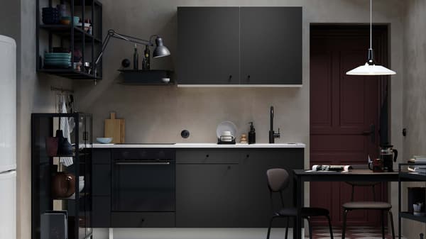A black KONXHULT kitchen, in a dark modern room, complemented by beige tiles.