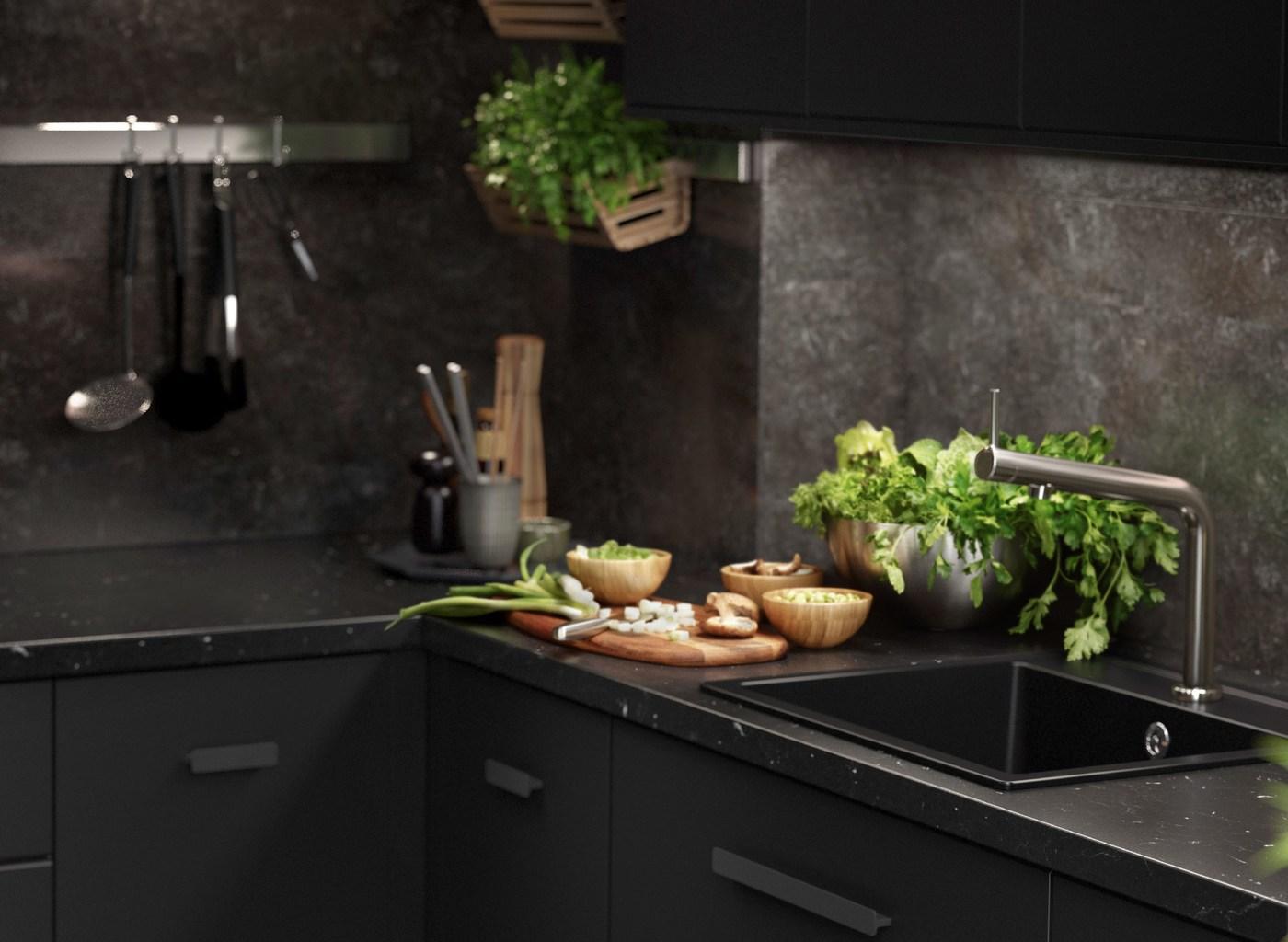 A black KUNGSBACKA kitchen with marble inspired features with kitchen utensils and fresh herbs.