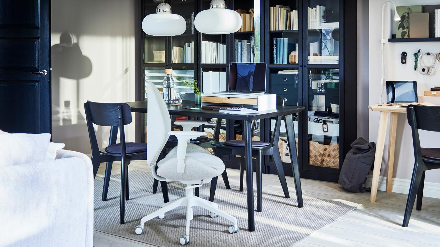 A black LISABO dining table with four chairs around it in front of glass-door bookcases, set up for work with a laptop.