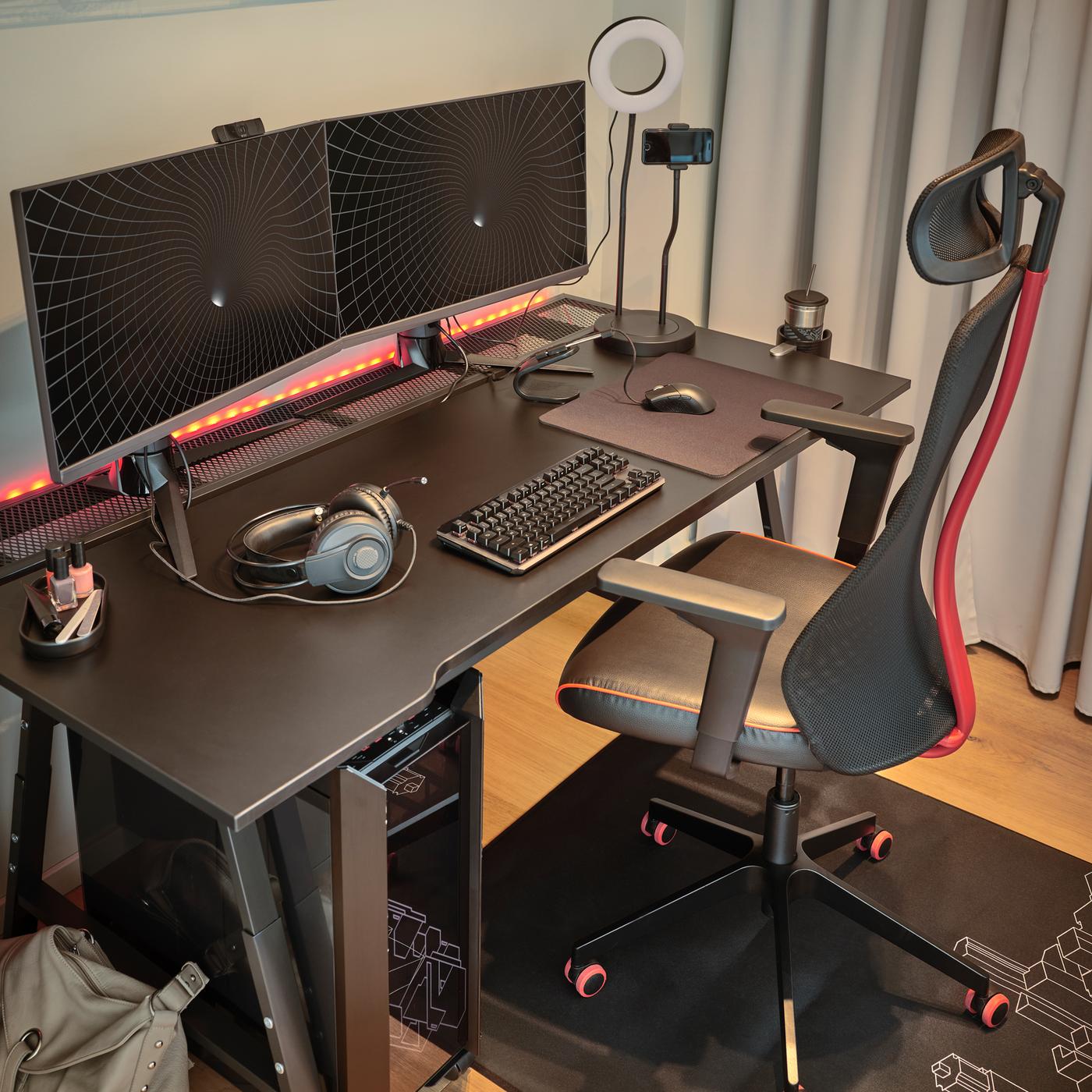 A black MATCHSPEL gaming chair and UTESPELARE gaming desk with a grey curtain on one side and two monitors on top.
