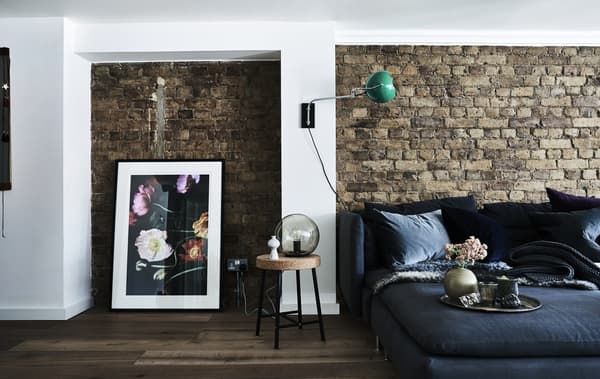 A black sofa against an exposed brick wall, next to a large picture leaning against the wall.