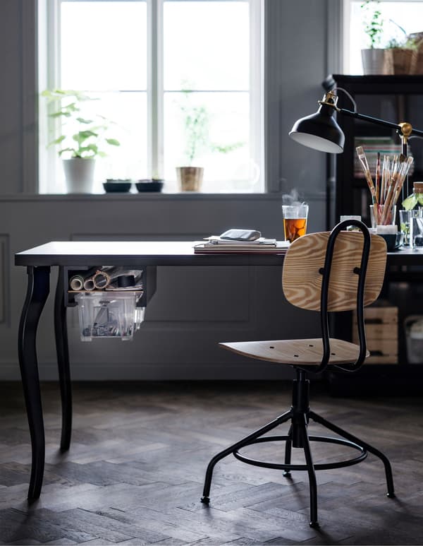 A black table with a DIY drawer is being used as a desk for a home office workspace.
