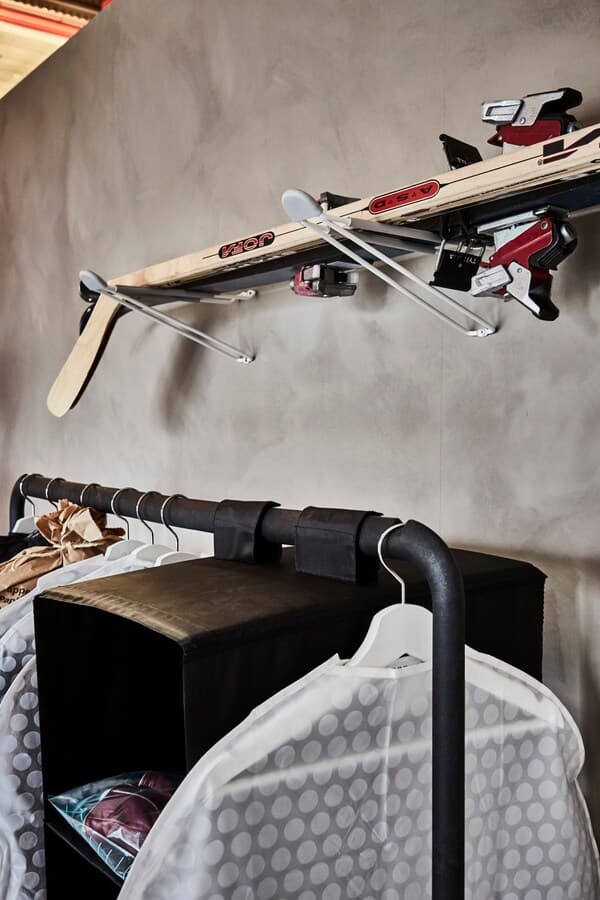 A black TURBO clothes rack with clothes covers attached, with two hooks above it on which skis rest