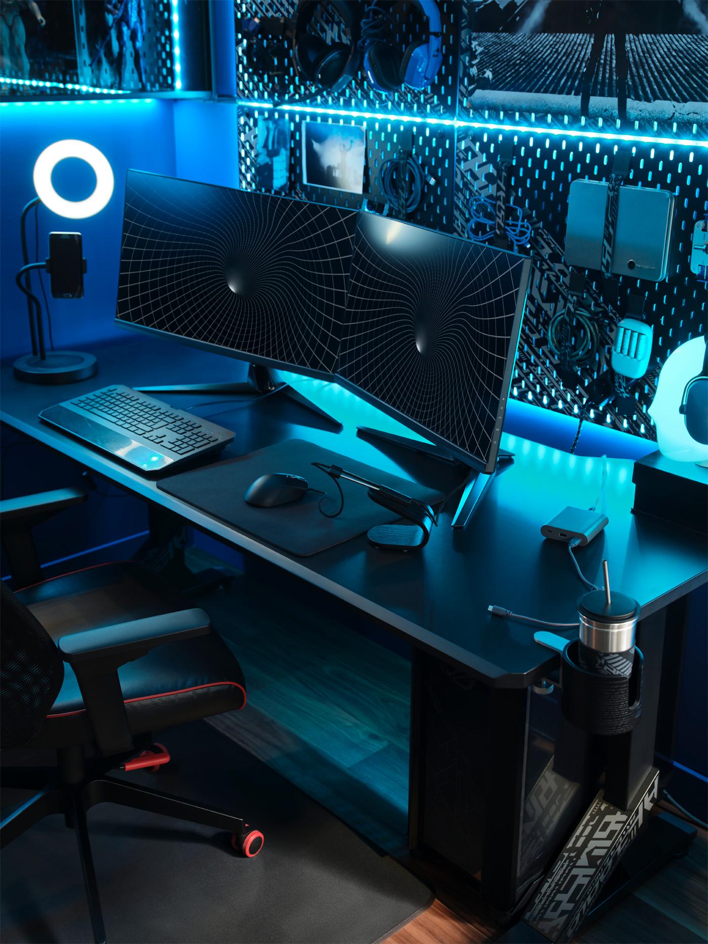 A black UPPSPEL gaming desk with two monitors, a ring light and keyboard on top and a pegboard holding gear behind it.