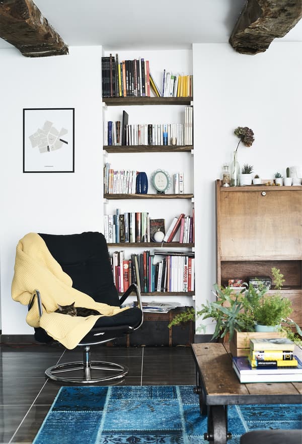 A black vintage IKEA swivel chair with yellow throw tossed onto it in an white walled, open airy living space.