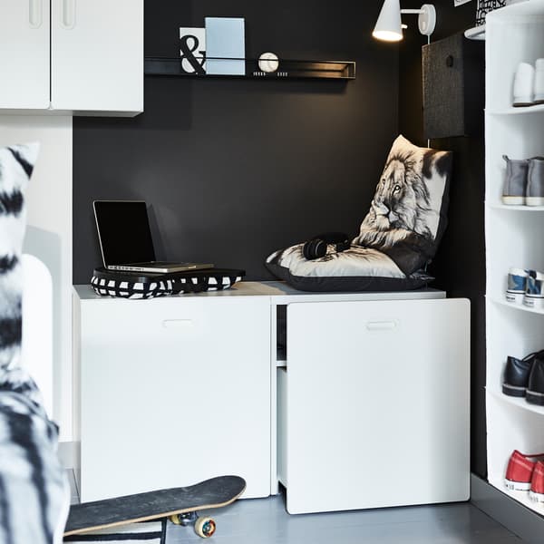 A black wall, a white wall cabinet, white toy boxes, a black shelf and a skateboard.