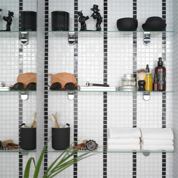 A black/white striped bathroom tile wall where 3 glass shelves are mounted and store towels, decorative items, and more.
