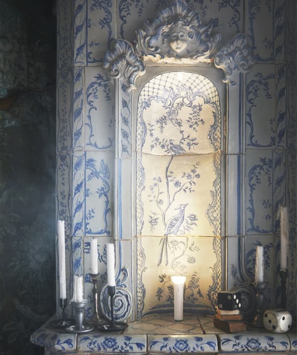 A blue and white Delftware pottery-style fireplace surround with candles and an illuminated torch on top.