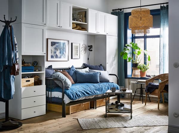 A blue and white studio apartment with the white PLATSA wardrobe arranged around a sleeping/living room zone.
