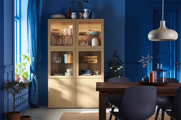 A blue dining room with a natural wood storage cabinet with plates, cups, and bowls inside