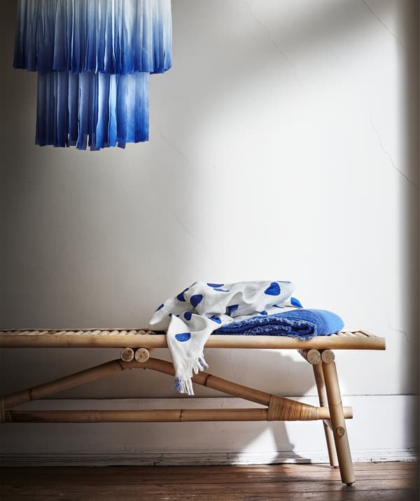 A blue fabric lampshade hanging above a rattan bench.