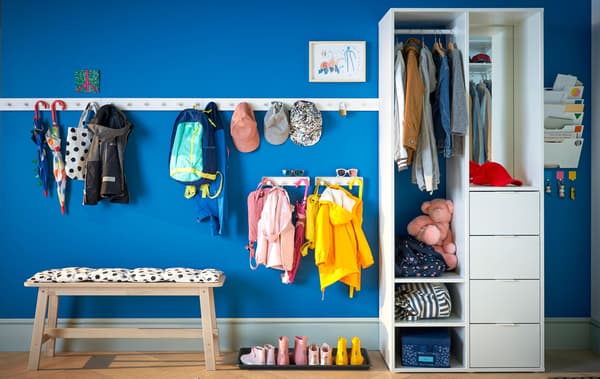 A blue hallway with coat racks, a bench and wardrobe storage.