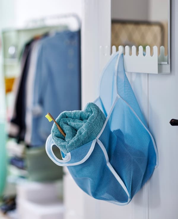 A blue mesh bag holding a towel and a toothbrush hangs from hooks on a GARNES mirror.