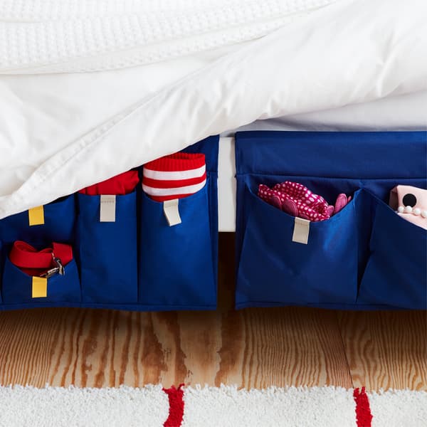 A blue MÖJLIGHET textile bed pocket for good-to-have storage hung on the side of a bed.