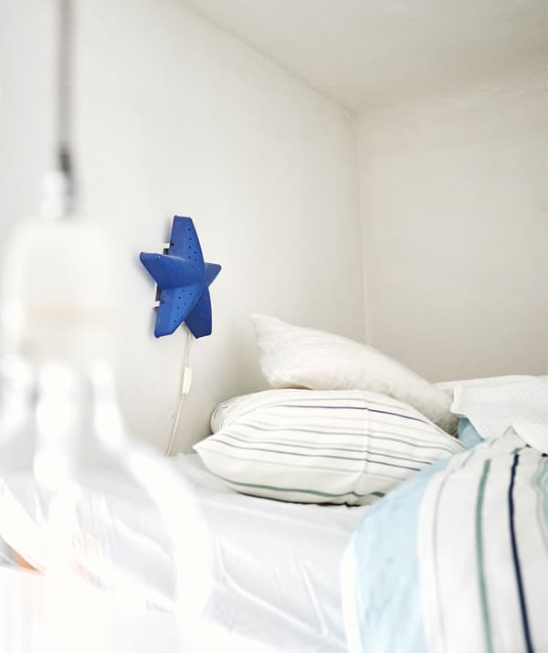 A blue star-shaped lamp on a wall above a bed with patterned textiles.